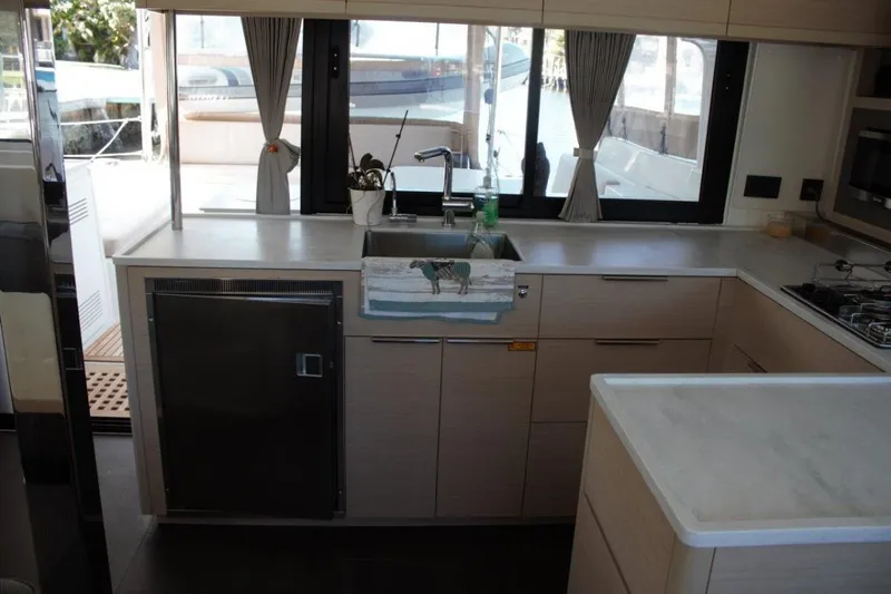 Jungle Goddess Yacht Photos Pics Modern kitchen interior on a 2022 Lagoon 46 yacht, featuring sleek cabinetry and large windows.