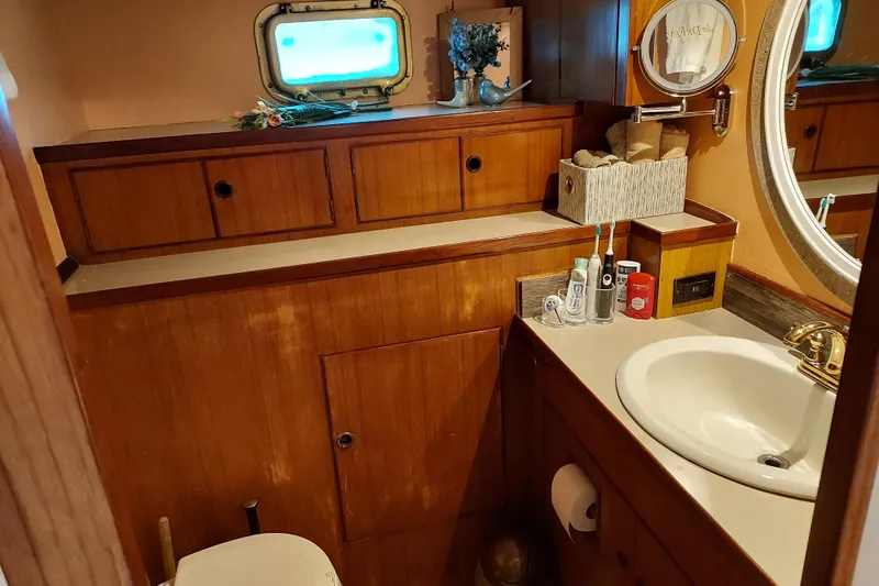 Noelani Yacht Photos Pics Bathroom interior of 1982 DeFever 52 Offshore Cruiser with wooden cabinetry and porthole window.