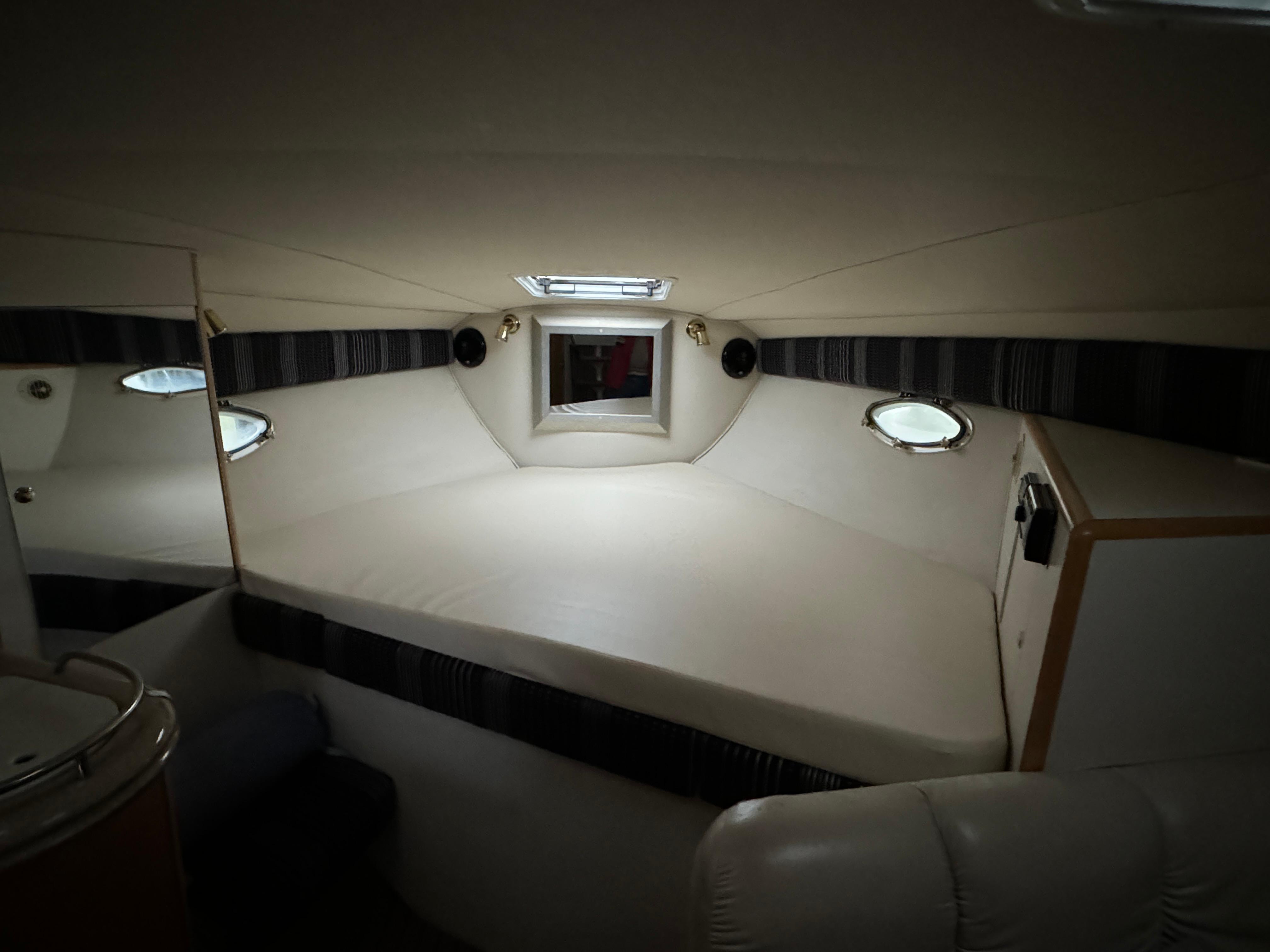 2003 Larson 330 CABRIO cabin interior with bed, portholes, and overhead lighting.