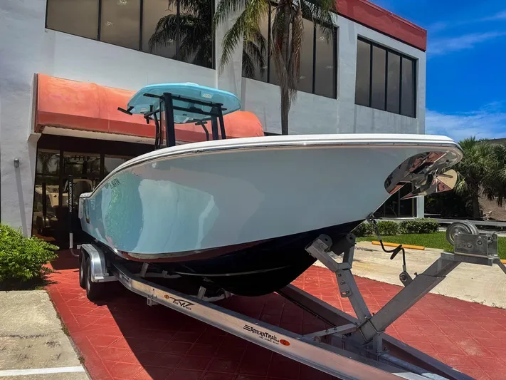  Yacht Photos Pics 2024 Tidewater 256 Adventurer boat on trailer outside a building, under clear blue sky.