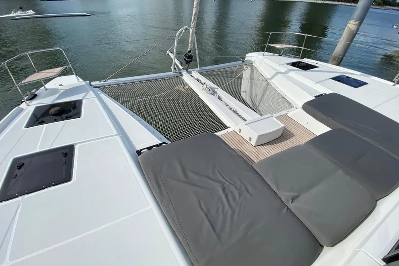  Yacht Photos Pics 2022 Lagoon 50 catamaran deck with cushioned seating and netting over water.