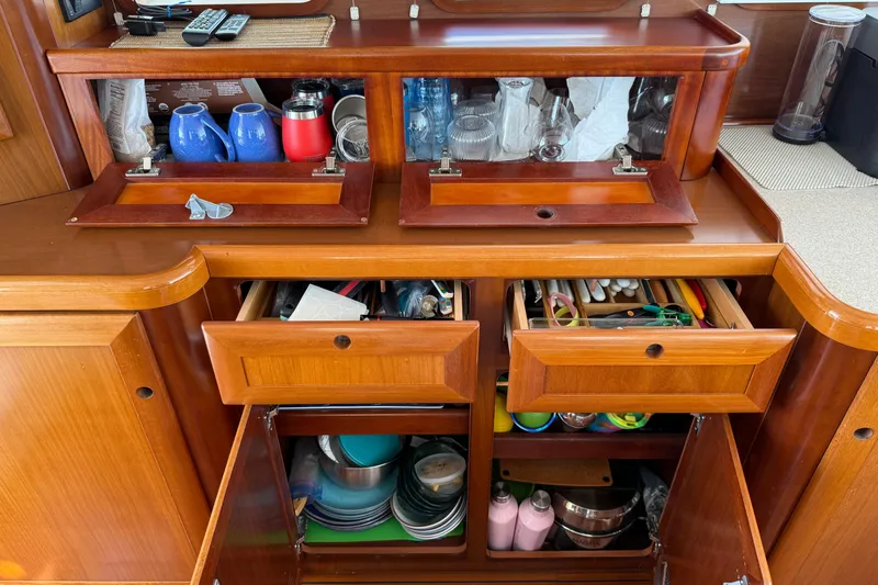 All At Sea Yacht Photos Pics Wooden kitchen storage on 2007 Beneteau Swift Trawler 42, featuring drawers and cabinets with utensils and dishes.