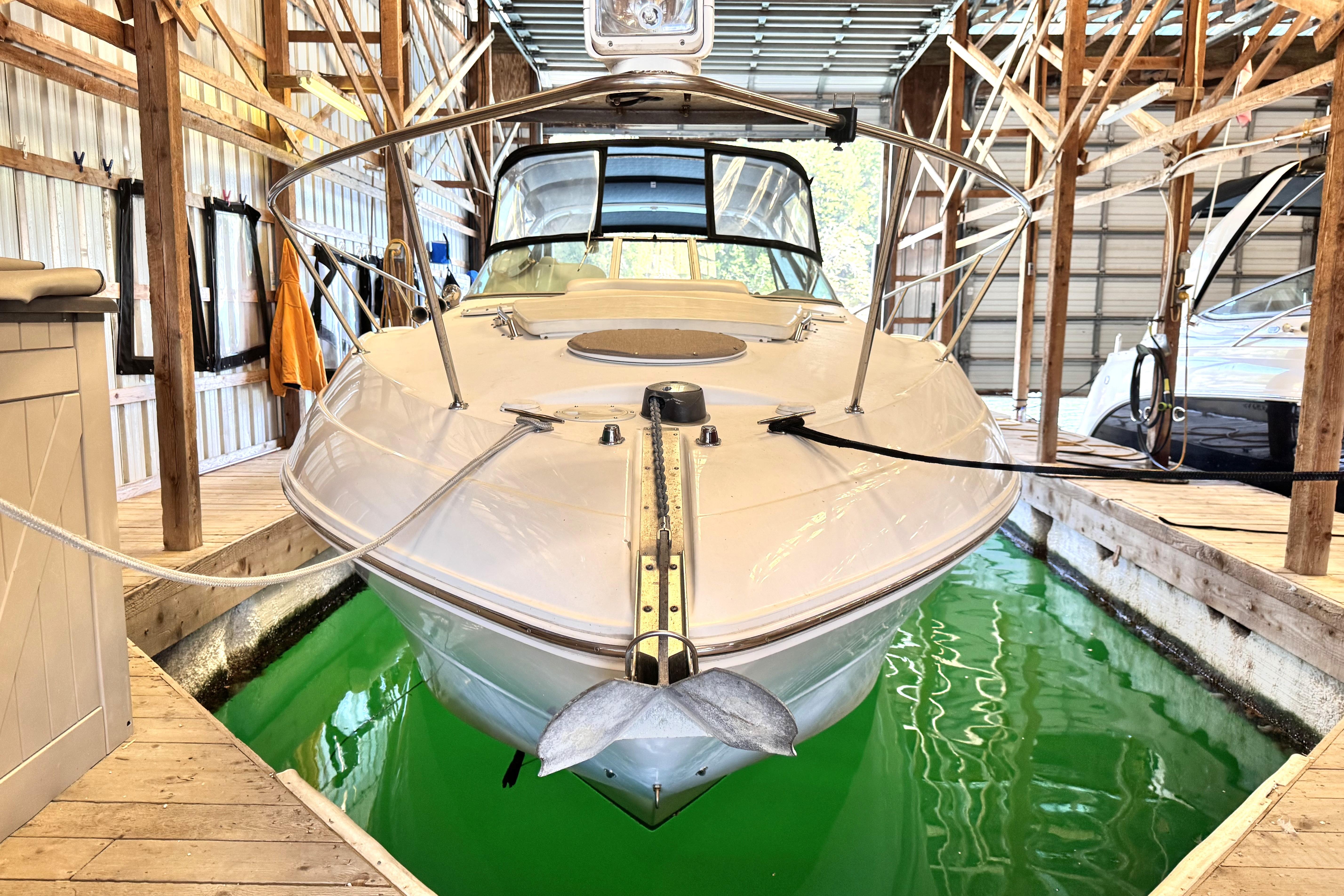 2002 Larson Cabrio 310 boat docked in a wooden boathouse with green water.