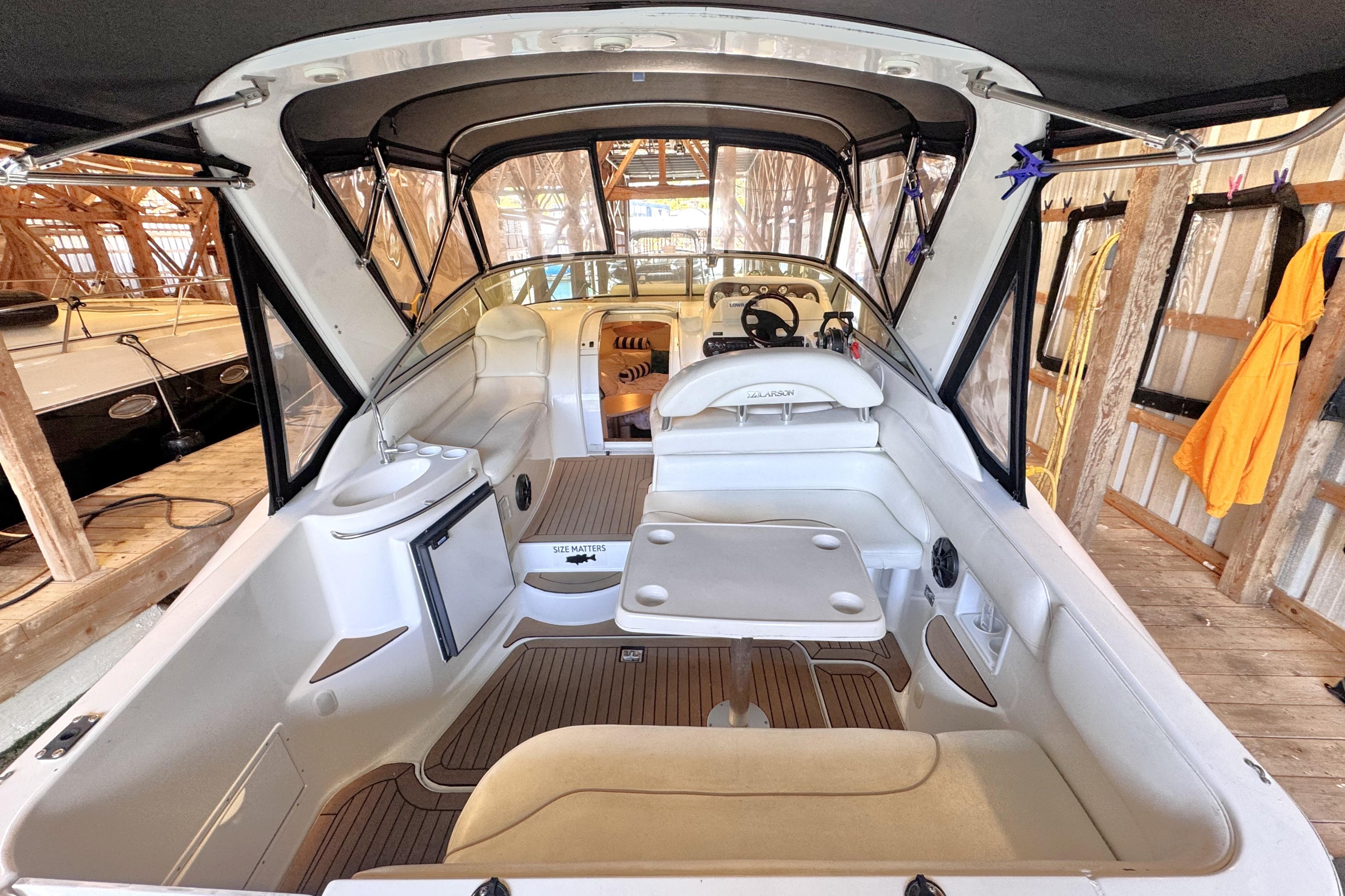 2002 Larson Cabrio 310 boat interior with seating, table, and helm in a wooden dock.