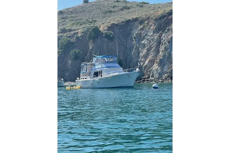 Fisher Folly IV Yacht Photos Pics 1988 Offshore Yachts 48 Yachtfisher anchored near rocky coastline.