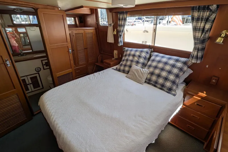 Fisher Folly IV Yacht Photos Pics Cozy bedroom in 1988 Offshore Yachts 48 Yachtfisher with plaid accents and wooden cabinetry.
