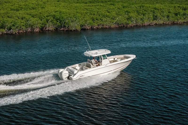  Yacht Photos Pics 2019 Boston Whaler 330 Outrage cruising on a scenic waterway near lush greenery.