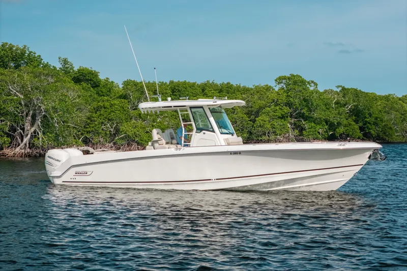  Yacht Photos Pics 2019 Boston Whaler 330 Outrage boat on calm water near lush green shoreline.