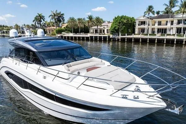 Endless Summer Yacht Photos Pics Luxurious 2020 Princess V55 yacht cruising near waterfront homes, under a clear blue sky.