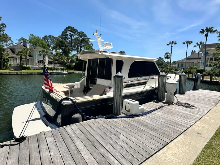 Yacht Photos Pics 2022 Back Cove 372 yacht docked by waterfront homes, clear sky, and lush greenery.