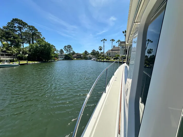  Yacht Photos Pics 2022 Back Cove 372 yacht cruising on a scenic, tree-lined waterway under a clear blue sky.