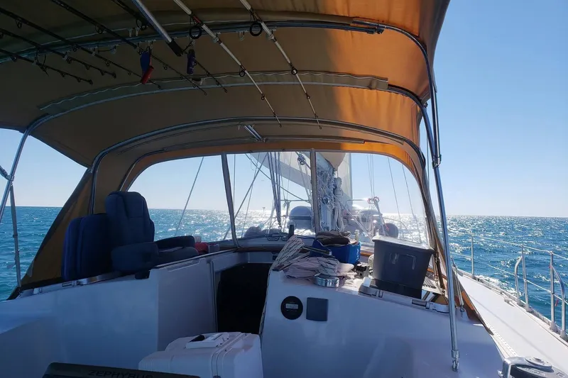 Zephyrus Yacht Photos Pics 1991 Beneteau 500 Oceanis sailboat cockpit with canopy, sailing on a sunny ocean.