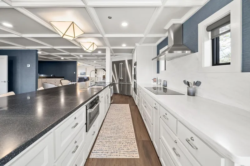 Shine Down Yacht Photos Pics Luxurious modern kitchen with sleek white cabinetry and dark countertops, featuring elegant lighting fixtures.