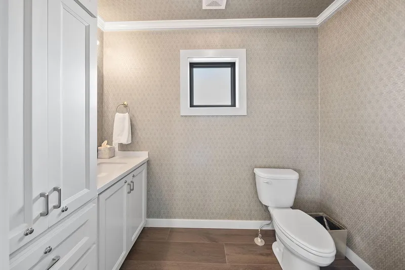 Shine Down Yacht Photos Pics Modern bathroom with white cabinetry, toilet, and patterned wallpaper, featuring a small window.
