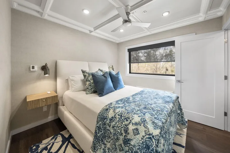 Shine Down Yacht Photos Pics Modern bedroom with blue accents, featuring a cozy bed, ceiling fan, and natural light.
