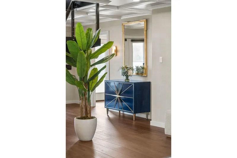 Shine Down Yacht Photos Pics Modern interior with blue cabinet, gold mirror, and potted plant on wooden floor.