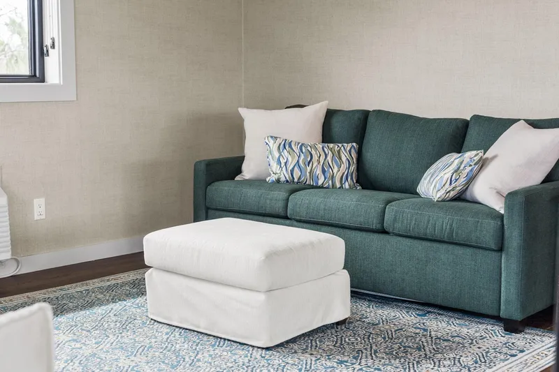 Shine Down Yacht Photos Pics Cozy living room with teal sofa, patterned pillows, and white ottoman on a decorative rug.