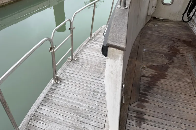 Qui-si-sana Yacht Photos Pics Wooden deck of 1989 Jefferson 52 Victory boat with metal railings by the water.