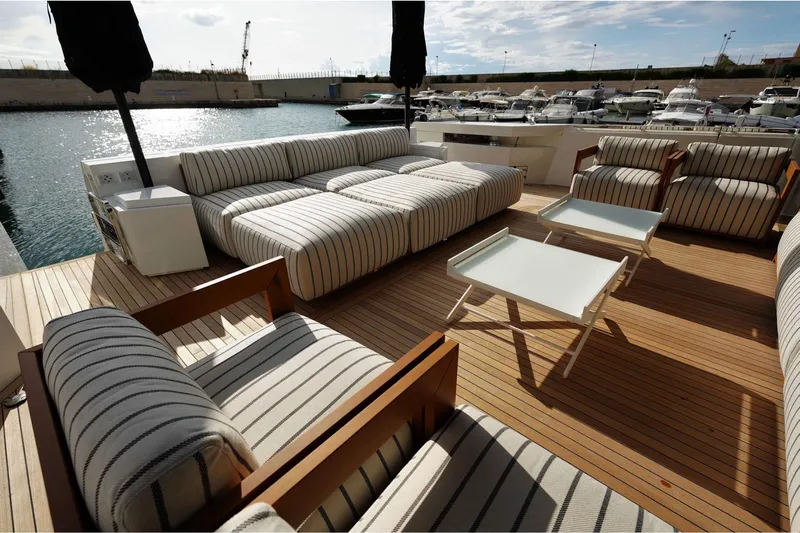  Yacht Photos Pics Luxurious deck seating on 2024 Arcadia Yachts A85, featuring striped cushions and wooden flooring.