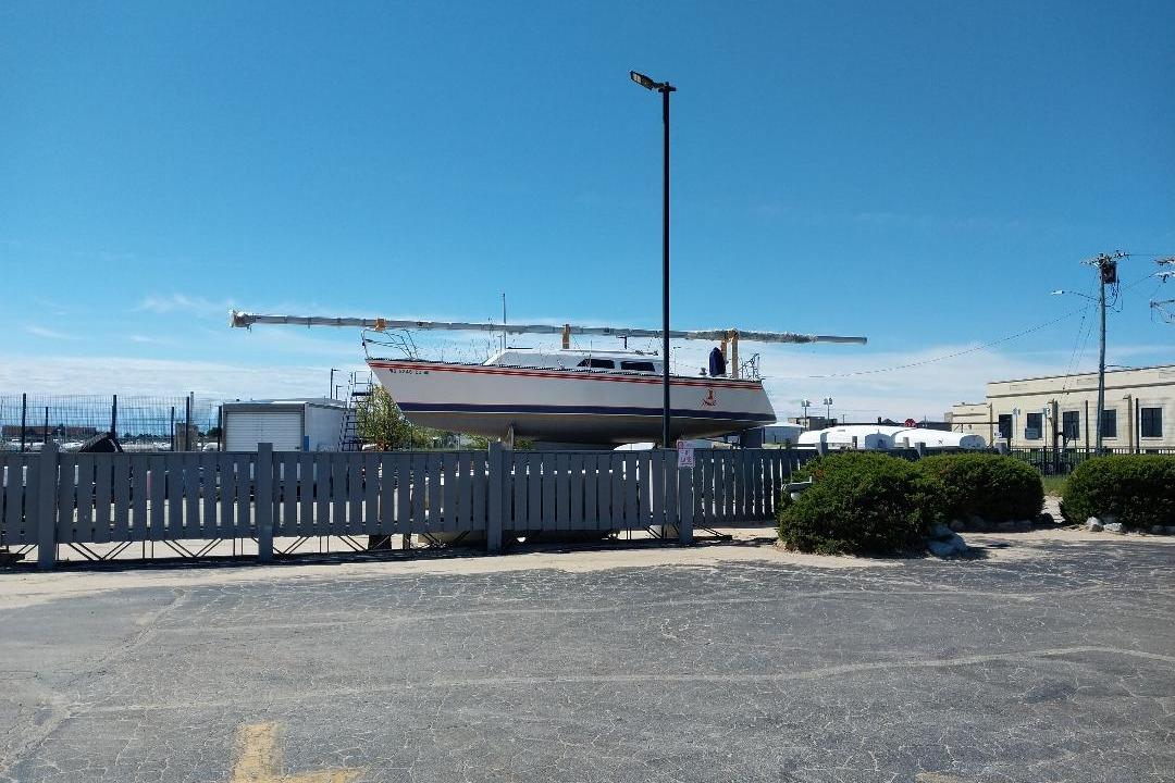 1983 Express 30 sailboat on land, behind a fence, under a clear blue sky.