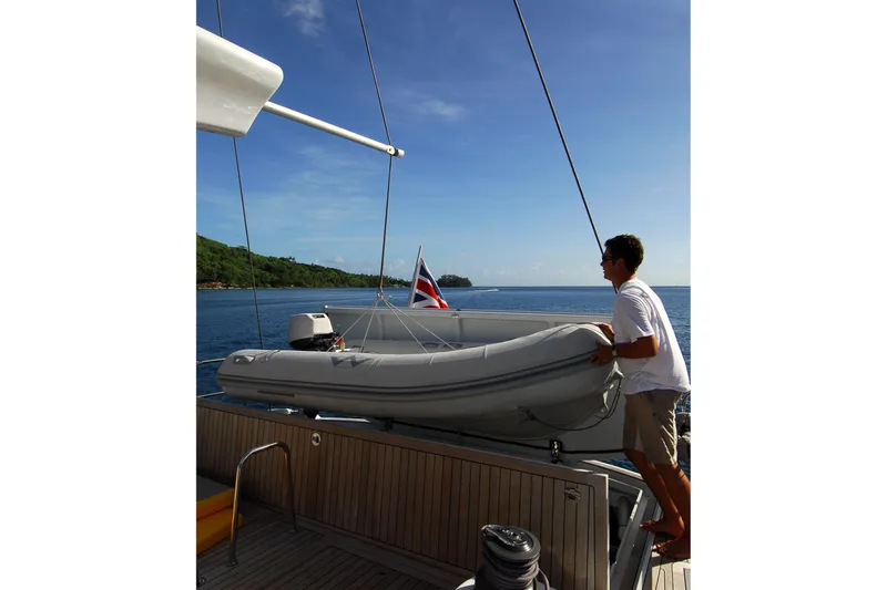 Whimsy Yacht Photos Pics Man handling dinghy on Vaudrey Miller 78 yacht, 2005, with scenic ocean backdrop.