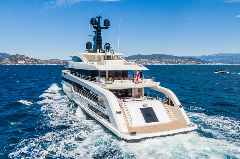 Rio Yacht Photos Pics Luxurious 2022 CRN 62m yacht cruising on blue ocean with scenic coastal backdrop.