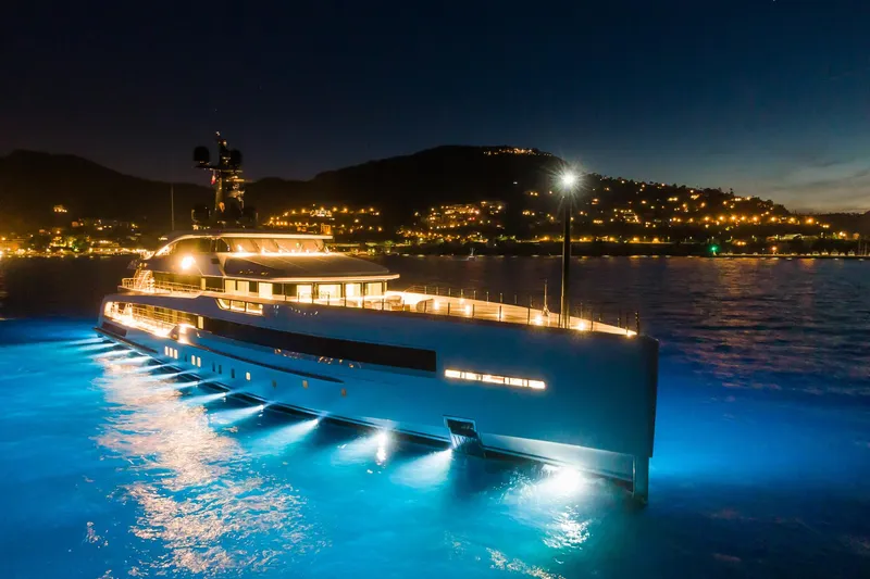 Rio Yacht Photos Pics Luxurious 2022 CRN 62m yacht illuminated at night, docked near a scenic coastline.