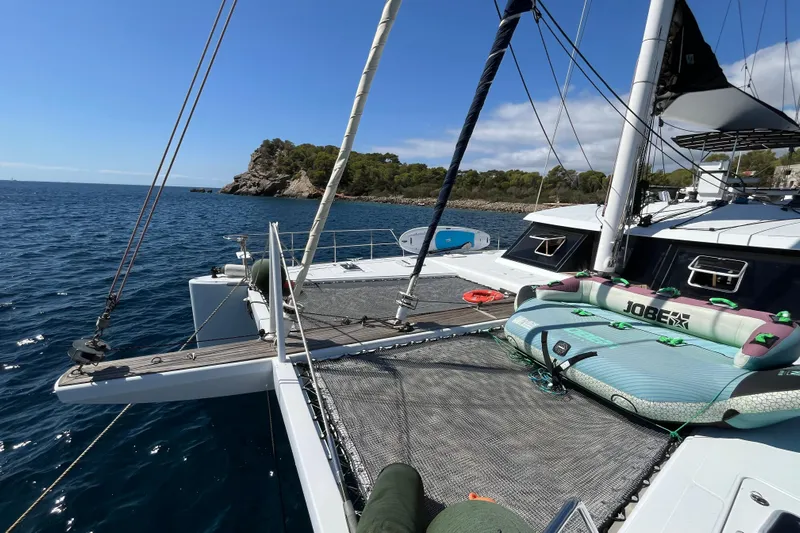 Sunreef 60 Yacht Photos Pics Sunreef 60 catamaran from 2005 anchored near a rocky coastline, featuring water sports equipment.