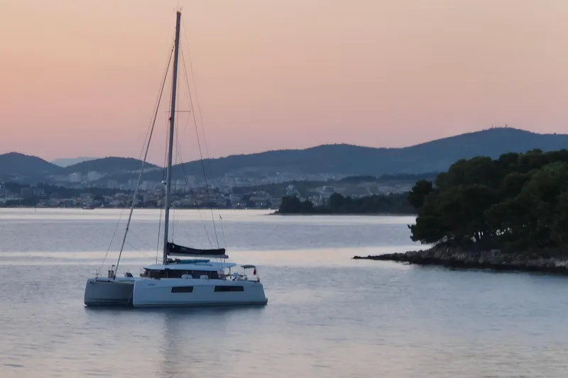 Double Memory Yacht Photos Pics 2023 Nautitech 44 catamaran sailing at sunset near a coastal landscape.