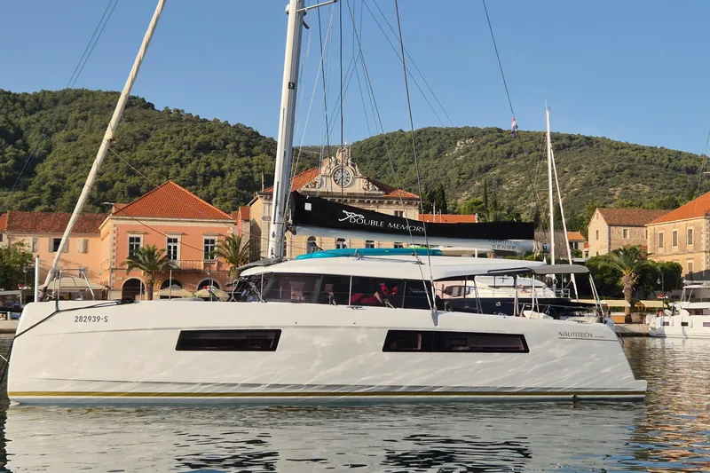 Double Memory Yacht Photos Pics 2023 Nautitech 44 catamaran docked in a scenic harbor with hillside backdrop.