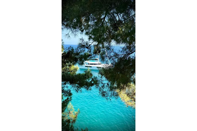 Double Memory Yacht Photos Pics Sailboat Nautitech 44, 2023 model, anchored in turquoise waters, framed by lush greenery.