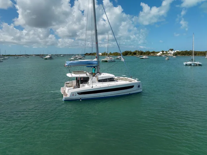 Cat Tales Yacht Photos Pics 2022 Bali 4.2 catamaran sailing in a serene bay under a partly cloudy sky.