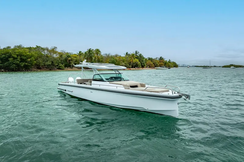  Yacht Photos Pics 2024 Axopar 37 Sun-Top boat cruising on clear waters near a tropical shoreline.