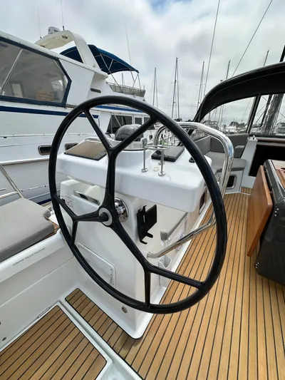 Edwina Yacht Photos Pics Steering wheel of a 2018 Jeanneau 54 yacht with teak deck and marina background.