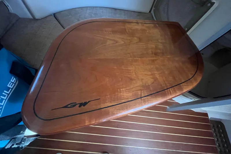 Revelry Yacht Photos Pics Wooden table inside 2003 Grady-White Express 330 boat cabin, featuring sleek design and logo.