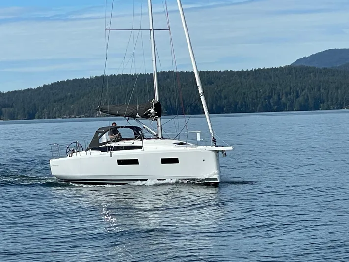  Yacht Photos Pics 2024 Jeanneau Sun Odyssey 350 sailing on calm waters with forested hills in the background.