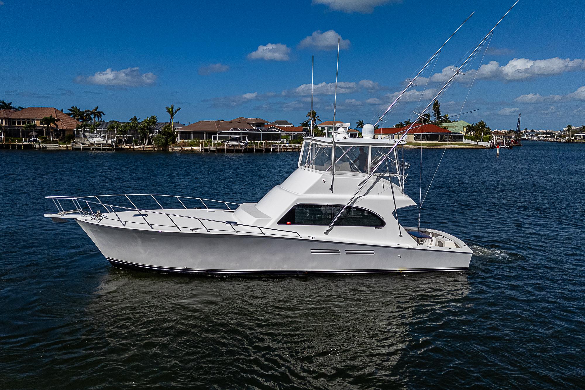 1999 Post 50 Convertible yacht cruising on a sunny day, waterfront homes in the background.