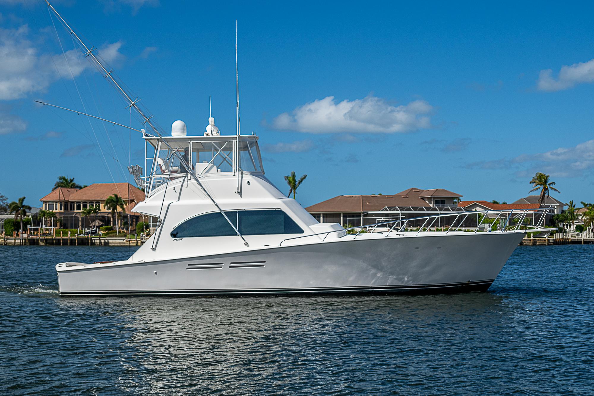 1999 Post 50 Convertible yacht cruising on a sunny day near waterfront homes.