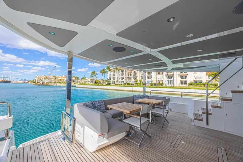 Hideout Yacht Photos Pics Luxurious 2025 Sunseeker 88 Yacht deck with seating, overlooking waterfront and modern buildings.