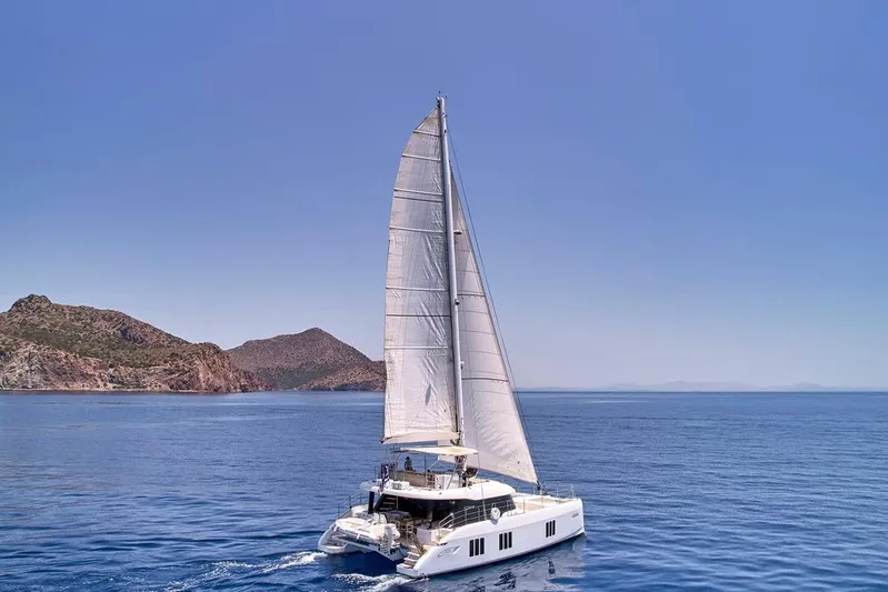Adara Yacht Photos Pics Sailing Sunreef 50 catamaran, 2020 model, cruising near rocky coastline under clear blue sky.