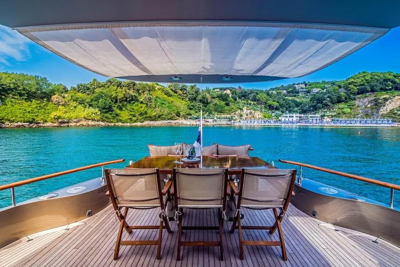  Yacht Photos Pics Luxury Acico 74 yacht deck with dining area, overlooking serene blue waters and lush green landscape.