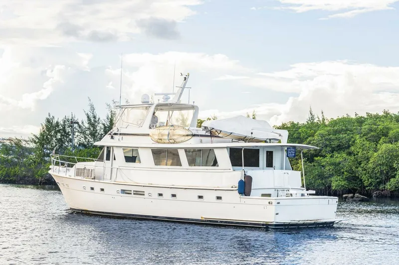  Yacht Photos Pics 1987 Hatteras 70 Cockpit Motor Yacht on calm water, surrounded by lush greenery.