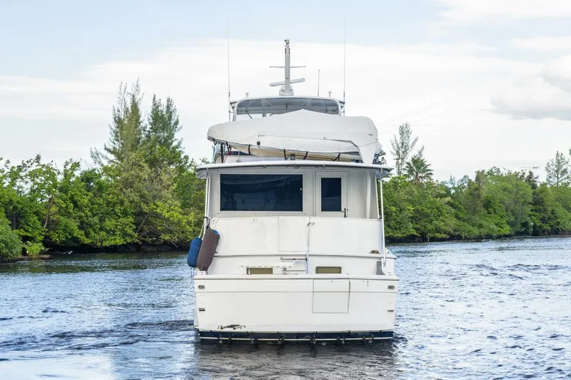  Yacht Photos Pics 1987 Hatteras 70 Cockpit Motor Yacht on a serene waterway, surrounded by lush greenery.