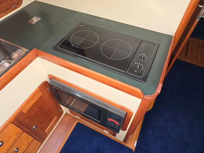 Lindy Yacht Photos Pics 2004 Legacy Sedan Flybridge kitchen with stove and microwave, featuring wood cabinetry and blue carpet.