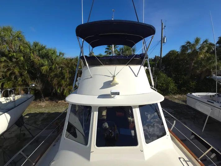 Lindy Yacht Photos Pics 2004 Legacy Sedan Flybridge boat with canopy, docked near lush greenery.