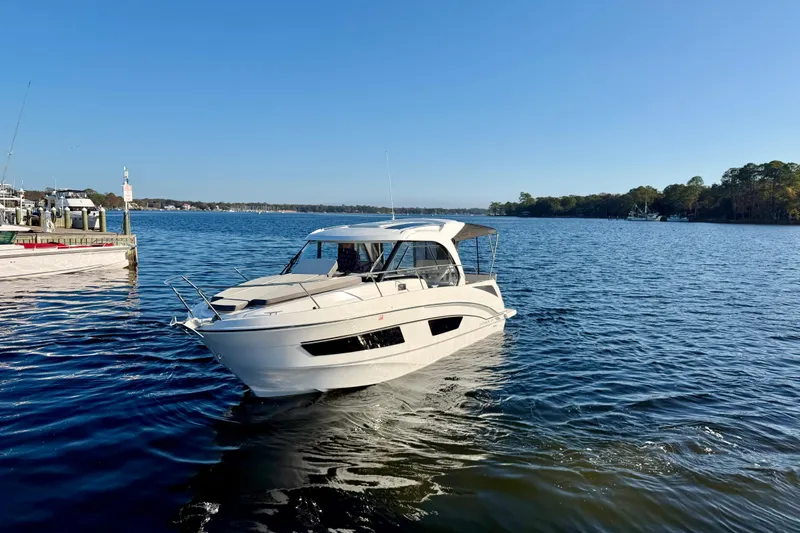 Yacht Photos Pics 2021 Beneteau Antares 9 cruising on a serene lake under a clear blue sky.