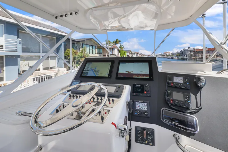 Legacy Yacht Photos Pics 2004 Cabo 40 Flybridge Convertible helm with navigation screens and controls, overlooking waterfront homes.