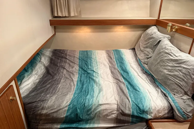 At Ease Yacht Photos Pics Cozy bedroom in 1997 Bayliner 47 Motoryacht with striped bedding and wooden accents.