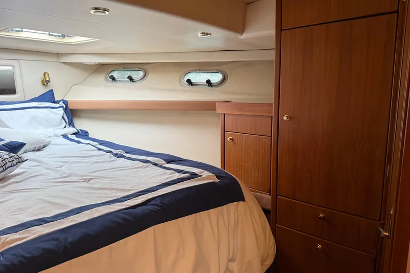 At Ease Yacht Photos Pics Luxurious cabin interior of 1997 Bayliner 47 Motoryacht with cozy bed and wooden cabinetry.