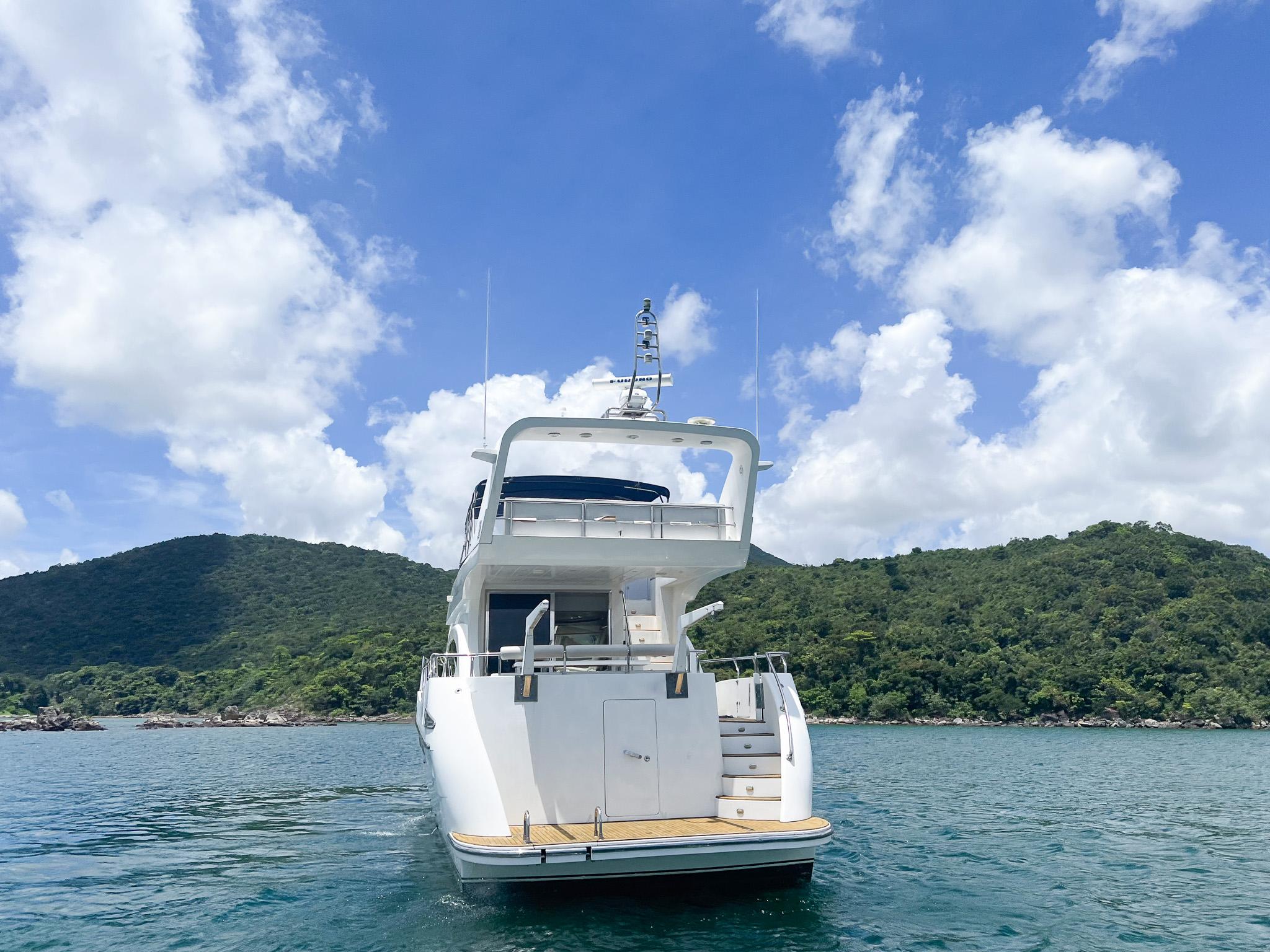 Luxury 2005 Vitech 65 yacht on serene water with lush green hills and blue sky.